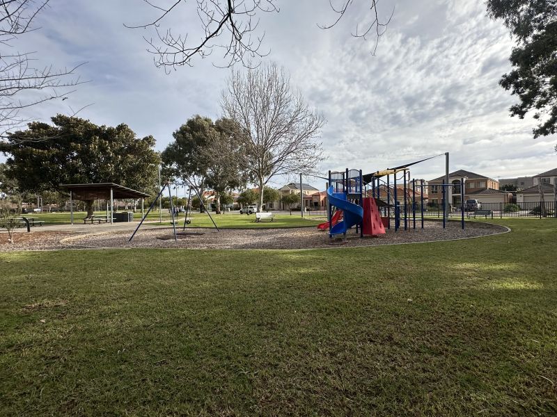 Image of playground facing Greenshield Place showing play structure, swing set, dog park, seating, shelter and picnic settings